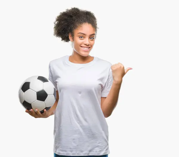 年轻美丽的美国黑人举行足球足球在孤立的背景指向和显示与拇指的一面微笑着快乐的脸 — 图库照片