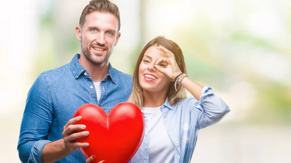 年轻夫妇在爱持有红色心脏在孤立的背景与快乐的脸微笑做 标志与手在眼睛看通过手指 — 图库照片