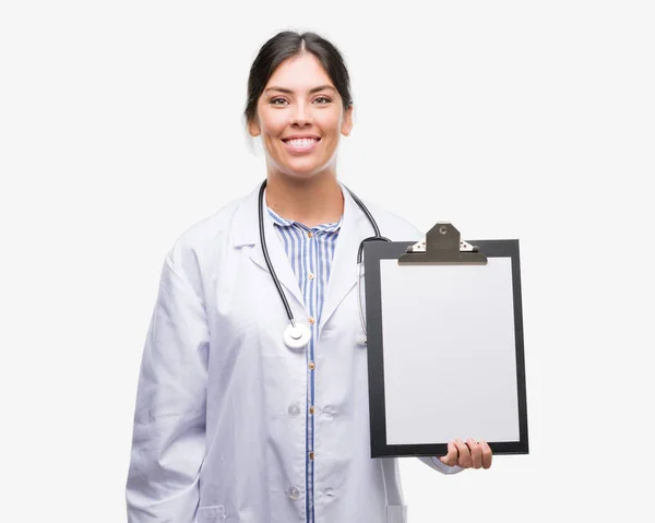 年轻的西班牙裔医生妇女持有剪贴板与一个幸福的脸站在微笑着自信的微笑显示牙齿 — 图库照片