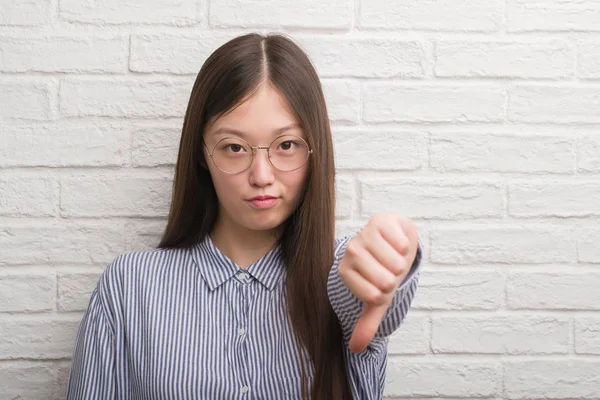 年轻的中国企业妇女在砖墙与愤怒的面孔 消极标志显示不喜欢与拇指下来 拒绝概念 — 图库照片