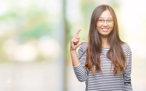 若いアジアの女性は 眼鏡をかけて分離背景笑顔と自信を持ってカメラを見ながら指でサイズ記号をやって手でジェスチャーします 測定概念 — ストック写真