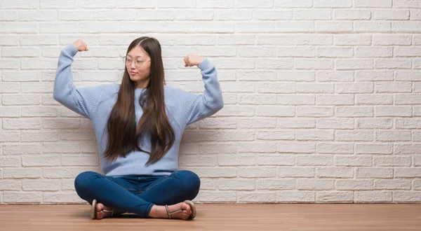 Молодая Китаянка Сидящая Полу Над Кирпичной Стеной Показывает Мускулы Рук — стоковое фото