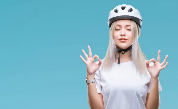 若いブロンドの女性の身に着けているサイクリスト セキュリティ ヘルメット孤立の背景の上を緩めて指で瞑想ジェスチャーをやって閉じた目を浮かべてします ヨガの概念 — ストック写真