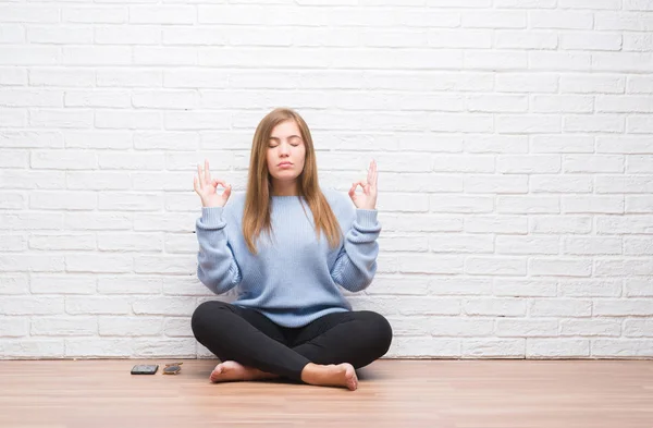 若い成人女性に座って秋白いレンガの壁の上に床リラックスして瞑想の指ジェスチャーをやって閉じた目と笑顔します ヨガの概念 — ストック写真