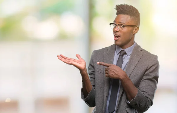 Young african american business man over isolated background amazed and smiling to the camera while presenting with hand and pointing with finger.