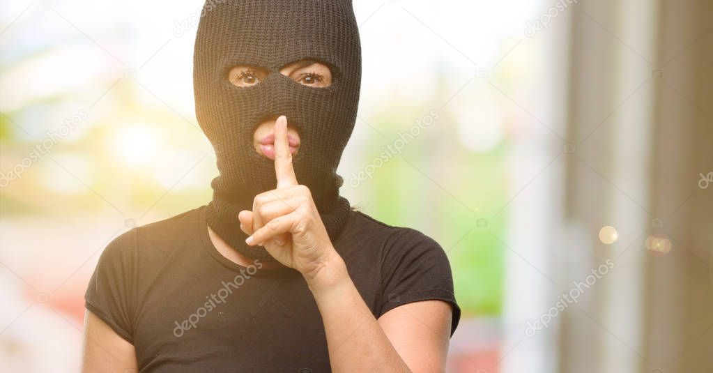 Burglar terrorist woman wearing balaclava ski mask with index finger on lips, ask to be quiet. Silence and secret concept