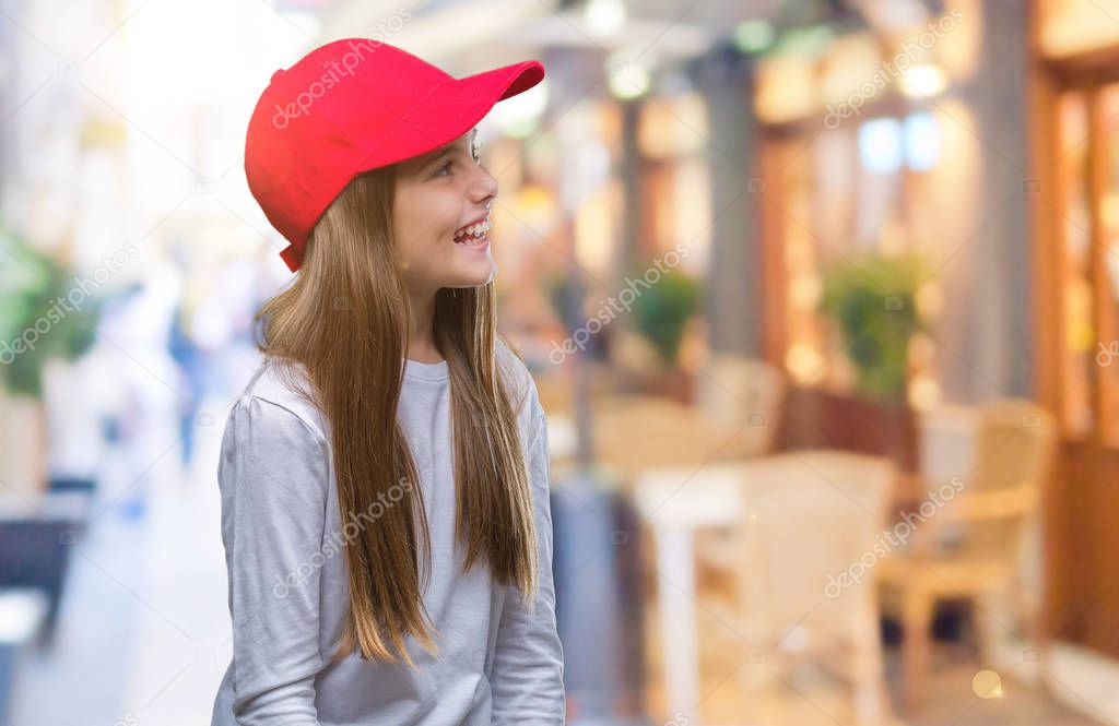 Young beautiful girl wearing red cap isolated background looking away to side with smile on face, natural expression. Laughing confident.