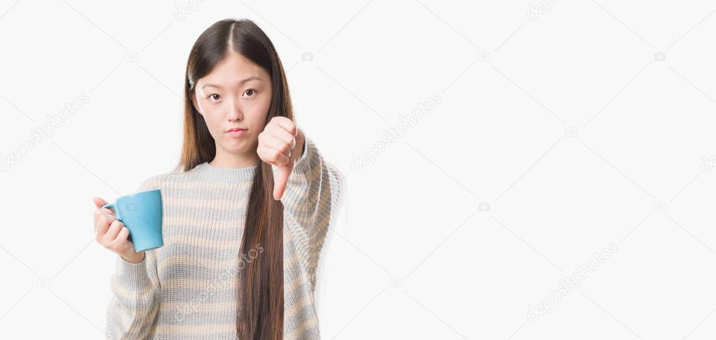 Young Chinese woman over isolated background driking cup of coffee with angry face, negative sign showing dislike with thumbs down, rejection concept