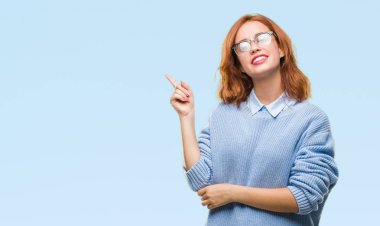 Kameraya bakarak yan el ve parmak ile işaret izole arka yüzünde, kocaman bir gülümseme ile kış kazak giyen genç güzel kadın.