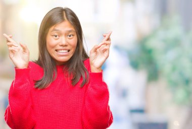 Umut ve gözleri kapalı geçiş parmaklarıyla gülümseyen izole arka plan üzerinde kış kazak giyen genç Asyalı kadın. Şans ve batıl kavramı.