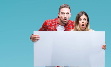 Genç çift birlikte boş afiş izole arka plan üzerinde bir sürpriz yüz, korkuyor ve heyecanlı korku ifadesi ile şok korkmuş holding