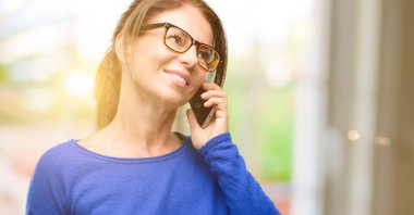 Yün kazak ve gözlük bir smartphone cep telefonu kullanarak konuşmak mutlu orta yaş kadın