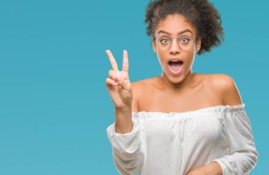 Mutlu yüz zafer işareti yaparken kameraya göz kırpıyor ile gülümseyen izole arka plan üzerinde gözlük takan genç afro Amerikalı kadın. İki numaralı.