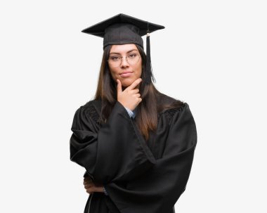 Giyen genç İspanyol kadın kap ve Tekdüzen seyir emin çapraz kollar ve çeneme kaldırdı el ile gülümseme ile kameraya mezun oldu. Pozitif düşünce.