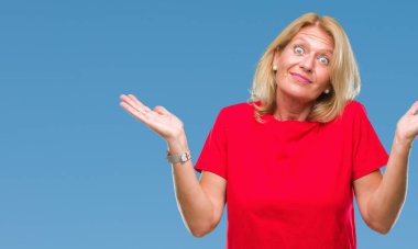 Orta yaş sarışın kadın izole arka plan clueless ve şaşkın bir ifadeyle kollar ve eller kaldırdı. Şüphe kavramı.