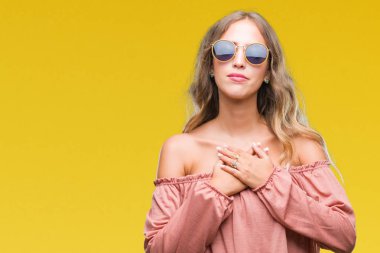 Güzel genç sarışın kadın ile gülümseyen izole arka plan üzerinde Retro güneş gözlüğü takıyor kapalı gözler ve yüzünde minnettar jest ile göğüs üzerinde eller. Sağlık kavramı.