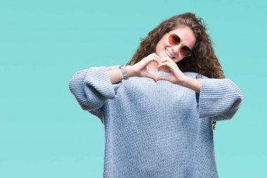 Güzel esmer kıvırcık saçlı Genç kız kalp simgesi ve elleriyle şekil gösterilen aşık gülümseyen izole arka plan üzerinde güneş gözlüğü takıyor. Romantik kavramı.