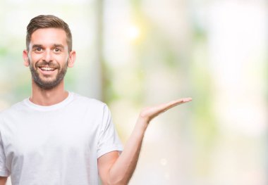 Genç yakışıklı adam neşeli sunulması ve kameraya bakarak avucunun ile işaret gülümseyen izole arka plan üzerinde.