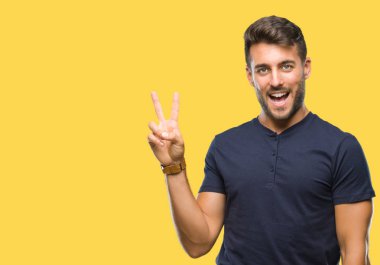 Mutlu yüz zafer işareti yaparken kameraya göz kırpıyor ile gülümseyen izole arka plan üzerinde genç yakışıklı adam. İki numaralı.