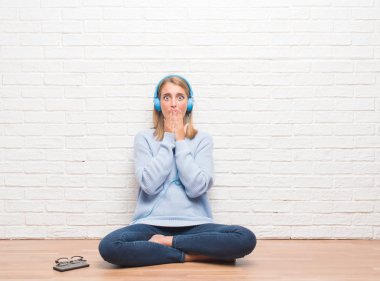 Hata, korku, sessizlik içinde gizli kavramı korkmuş ifade için utanç ile kapak ağız el ile kulaklık evde giyiyor kat dinleme müzik üzerinde oturan güzel genç kadın şok