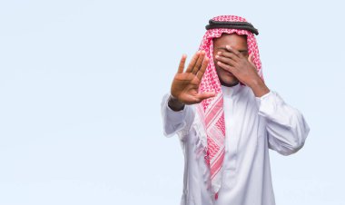 Genç Arap Afrika elleriyle gözlerini kapsayan izole arka plan üzerinde giyen geleneksel keffiyeh adam ve stop jest ile acı ve korku ifadesi. Utandım ve negatif kavramı.