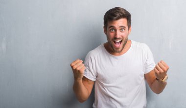 Gri grunge duvar kutluyor üzerinden yakışıklı delikanlı şaşırttı ve başarı için kaldırdı kollarını açarak hayret ve gözleri açık. Kazanan kavramı.