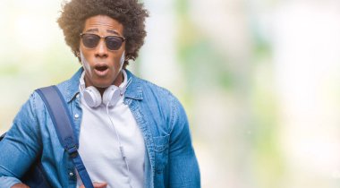Üzerinde kulaklık ve sırt çantası takmış Afro Amerikalı adam arka plan bir sürpriz yüz, korkuyor ve heyecanlı korku ifadesi ile şok korkmuş izole