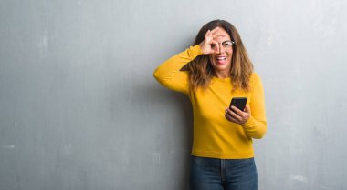 Mutlu yüz el parmaklarının arasından seyir göz üzerinde ok işaretiyle yapıyor gülümseyen ile akıllı telefon kullanan orta yaş İspanyol kadın