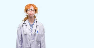 Komik surat ile yanakları şişirme Doktor üniforması giyen genç redhead kadın. Ağız ile hava, deli ifade şişirilmiş.