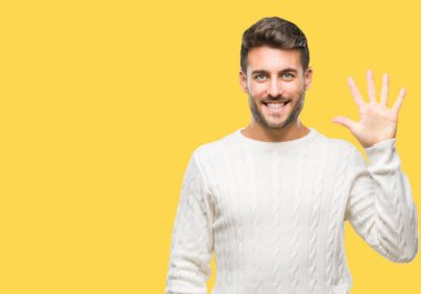 Gösterilen arka plan üzerinde kış kazak giyen genç yakışıklı adam izole ve parmakları ile işaret kendinden emin ve mutlu gülümseyerek süre beş numara.