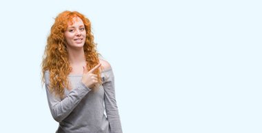 Genç Kızıl saçlı kadın neşeli bir gülümseme ile el ve parmak kadar kameraya bakarak yüzündeki mutlu ve doğal ifade ile yan ile işaret eden yüz.