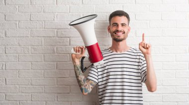 Genç Yetişkin holding megafon bir fikirle şaşırmış adam ya da gülen yüz, bir numara ile işaret parmağı soru