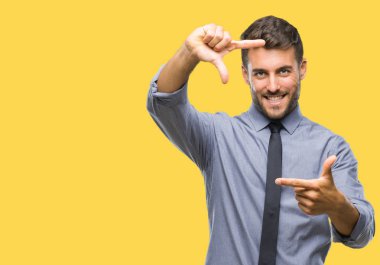 Genç yakışıklı iş adamı elle yapma çerçeve ve parmakları ile mutlu yüz gülümseyen izole arka plan üzerinde. Yaratıcılık ve Fotoğrafçılık kavramı.