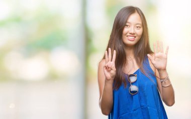 Genç Asyalı kadın gösterilen ve parmakları ile işaret izole arka plan üzerinde kendinden emin ve mutlu gülümseyerek süre sekiz numara.