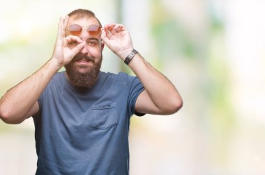 Genç beyaz hipster adam gülümsüyor, parmakları ile mutlu yüz üzerinden seyir göz el ile ok jest yapıyor izole arka plan üzerinde güneş gözlüğü takıyor.