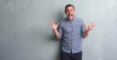 Gri grunge duvar kutluyor üzerinde beyaz delikanlı deli ve çığlık kaldırdı ve açık gözleri heyecanlı silah ile başarı için hayran. Kazanan kavramı