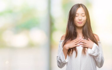 Genç Asyalı kadın ile gülümseyen izole arka plan üzerinde kapalı gözler ve yüzünde minnettar jest ile göğüs üzerinde eller. Sağlık kavramı.