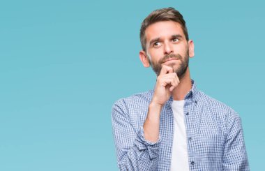 Çene düşünme hakkında soru, dalgın ifade üzerine el ile izole arka plan üzerinde beyaz t-shirt giyen genç yakışıklı adam. Düşünceli yüzüyle gülümsüyor. Şüphe kavramı.