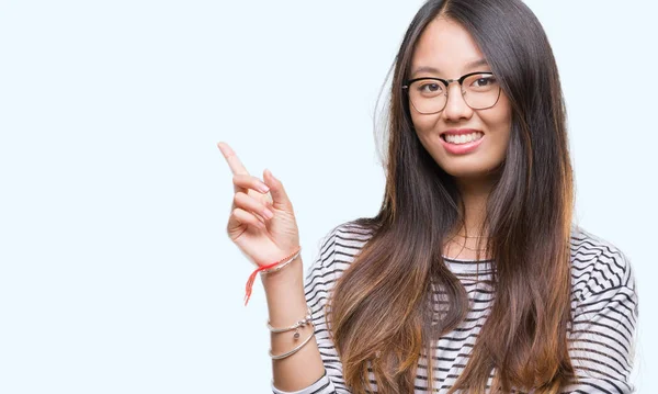 カメラを見て側に手と指で指している眼鏡の顔に大きな笑みを浮かべて隔離された背景に若いアジア女性 — ストック写真
