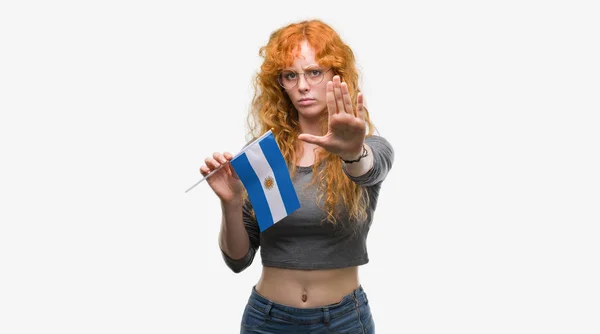 防衛ジェスチャー 深刻な自信を持って式に一時停止の標識を行うオープン手でアルゼンチンの旗を保持している赤毛の若い女性 — ストック写真