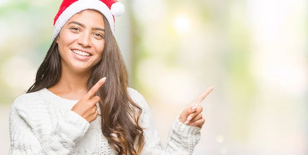 年轻的阿拉伯妇女戴着圣诞帽在孤立的背景下微笑着 看着相机指着两只手和手指的侧面 — 图库照片