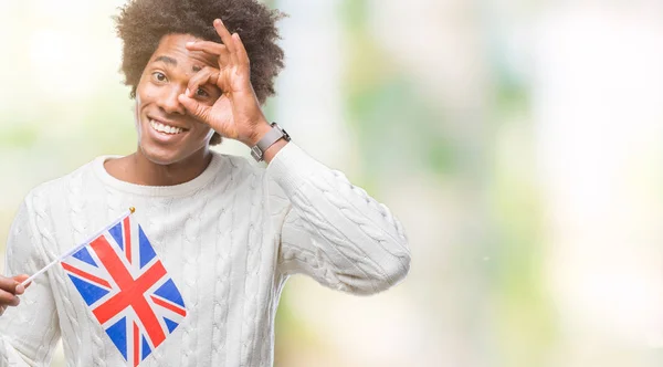 Afro american man flag of United Kingdom over isolated background with happy face smiling doing ok sign with hand on eye looking through fingers