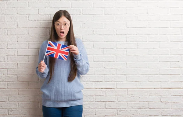 Joven Mujer China Sobre Muro Ladrillo Sosteniendo Bandera Inglaterra Asustada —  Fotos de Stock