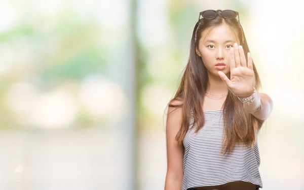年轻的亚洲妇女戴着太阳镜在孤立的背景下做停止唱歌与手掌的手 脸上带有否定和严肃手势的警告表达式 — 图库照片