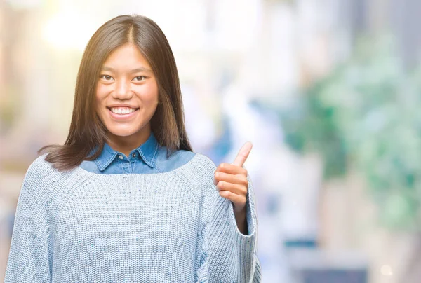 若いアジアの女性は 幸せな親指の手でジェスチャーを行う分離の背景に冬のセーターを着ています 成功を示すと カメラを見て式を承認します — ストック写真