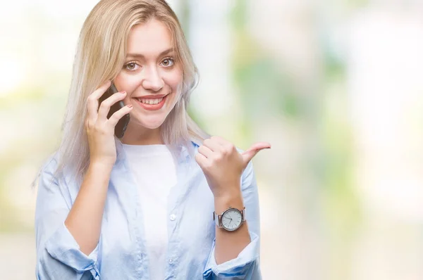 年轻的金发女人说话使用 Smarpthone 在孤立的背景下指向和显示与拇指向上微笑的一面与快乐的脸 — 图库照片