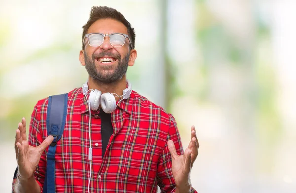 Üzerinde kulaklık ve sırt çantası giyiyor yetişkin İspanyol öğrenci adam arka plan deli izole ve deli bağırarak ve agresif ifade ve silah kaldırdı bağırıyor. Hayal kırıklığı kavramı.