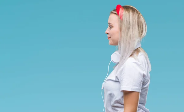 若いブロンドの女性の身に着けているヘッドフォン側を分離の背景に音楽を聴いてリラックスして自信を持って笑顔で自然の顔を持つプロファイル ポーズ — ストック写真
