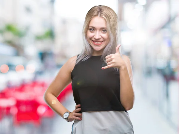 Young blonde woman over isolated background smiling doing phone gesture with hand and fingers like talking on the telephone. Communicating concepts.