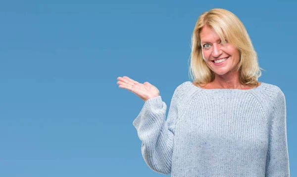 陽気な提示とカメラを見て手の手のひらで指している笑みを浮かべて分離の背景に冬のセーターを着て中年の金髪女性 — ストック写真